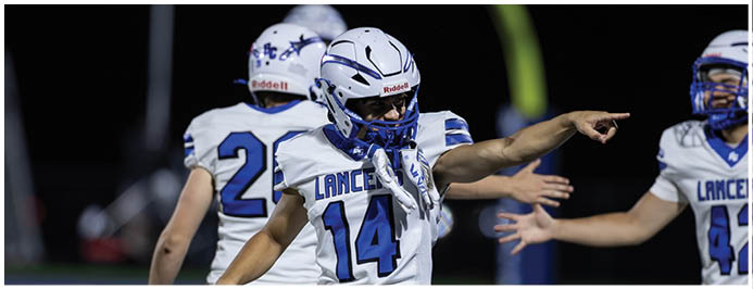 People in white and blue football uniforms are celebrating on a field during a game. Description generated by AI