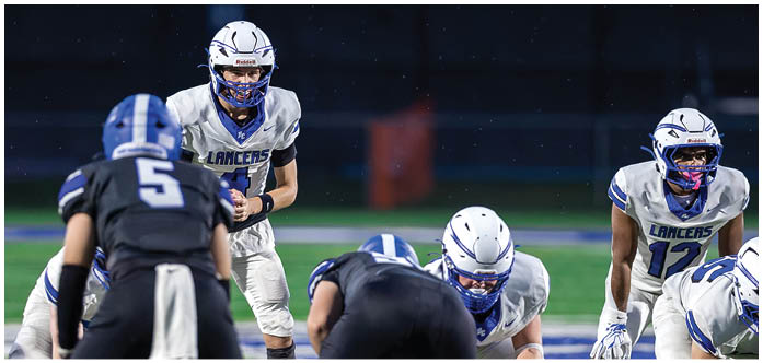People in football uniforms are lined up on a field preparing for a play during a game. Description generated by AI