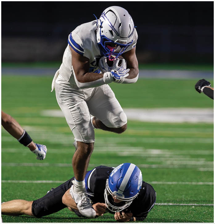 A person wearing a white football uniform and helmet is catching a football on a green field at night. Description generated by AI