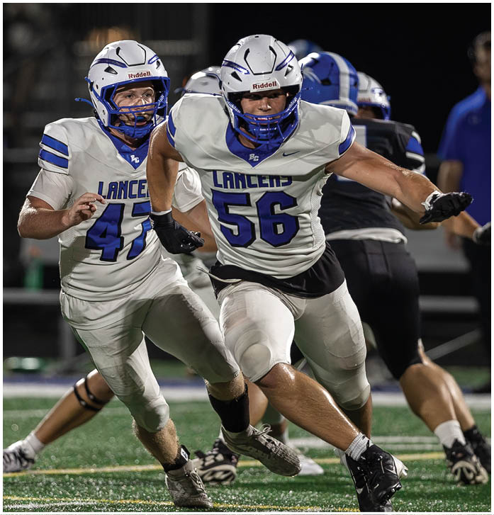 Two teams of people in football uniforms are actively engaged in a game on a field under stadium lights. Description generated by AI