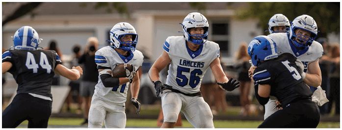 Four people in football uniforms are actively running on a grassy field during a game. Description generated by AI