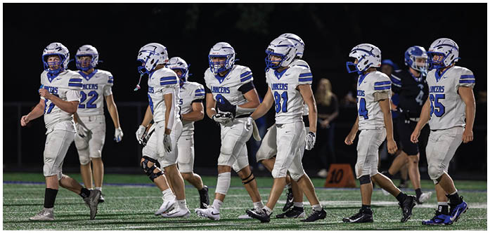 Several people wearing white football uniforms with blue helmets and the word “Lancers" on their jerseys are walking together on a field at night. Description generated by AI