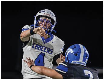 A person wearing a white football helmet with a blue and black design is visible at the bottom of the image against a black background. Description generated by AI