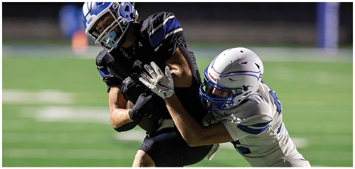 Two people in football uniforms are engaged in a tackle on a grassy field. Description generated by AI