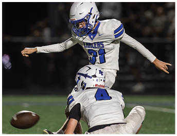 A person wearing a white football helmet with blue accents is shown from the side against a dark, blurred background. Description generated by AI