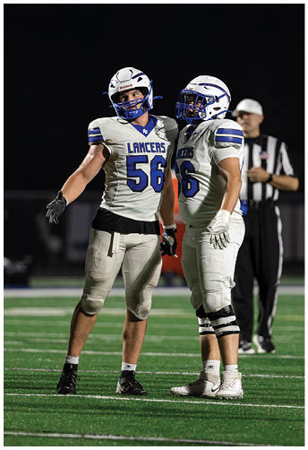 Two people wearing white football uniforms with blue numbers and the word LANCERS are standing on a field. Description generated by AI