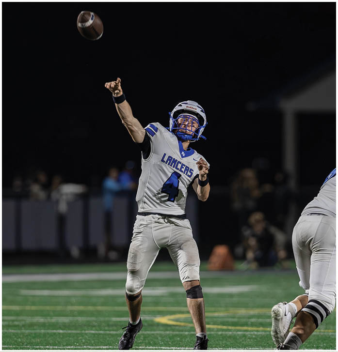 People wearing white football uniforms with blue accents are standing on a green field at night. Description generated by AI
