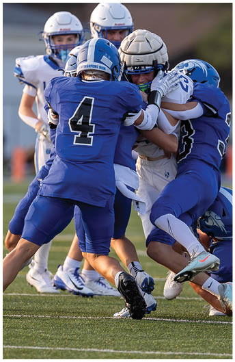 Several people in football uniforms and helmets are engaged in a close physical play on a field. Description generated by AI