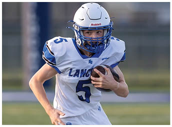 A person wearing a white football helmet and a white jersey with the number five is running while holding a football. Description generated by AI