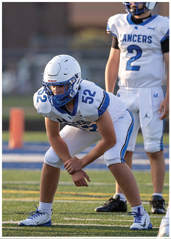 People in football uniforms are positioned on a field preparing for a play during a game. Description generated by AI