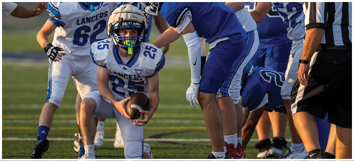 A group of people wearing football helmets and uniforms are gathered closely on a field, appearing to be in the middle of a game or practice. Description generated by AI