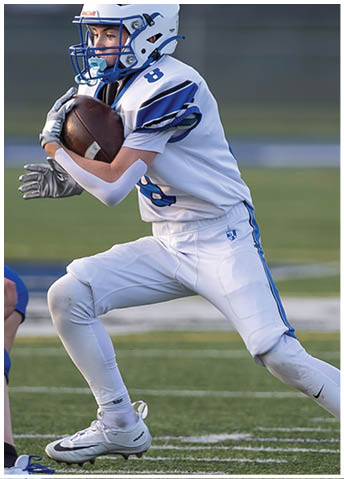 Two people in football uniforms are on a field with one person in blue reaching out toward the other person in white who is running away. Description generated by AI