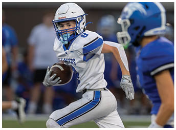 A person wearing a white football helmet and blue and white uniform is focused and appears to be in action during a game. Description generated by AI