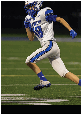 A person wearing white athletic pants with blue stripes and blue socks is running on a green sports field. Description generated by AI