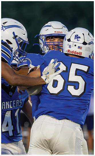 Three people wearing blue and white football uniforms are engaged in a game on a field. Description generated by AI