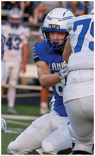 A group of people wearing football helmets and uniforms are on a field with blurred spectators in the background. Description generated by AI