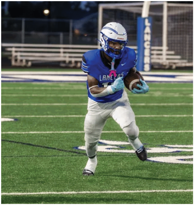 A person wearing a blue football uniform and white helmet is running on a football field while holding a football near a goalpost with “Lancers" written on the padding. Description generated by AI