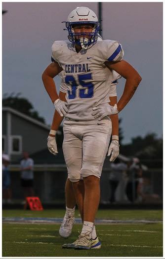 A person wearing a white football uniform with the word Central and the number 35 stands on a field at dusk with hands on hips. Description generated by AI