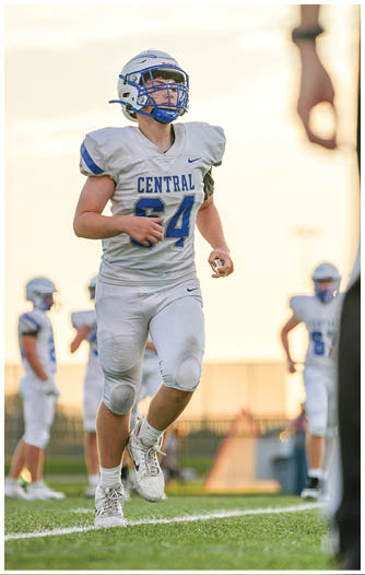 A person wearing a white football uniform with the word “CENTRAL" and the number 34 is running on a grassy field with other players in the background. Description generated by AI