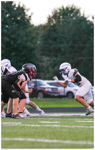 Several people in football uniforms are lined up facing each other on a field, preparing for a play during a game. Description generated by AI
