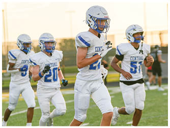 Several people wearing white athletic pants and cleats are running on a grass field marked with white lines. Description generated by AI