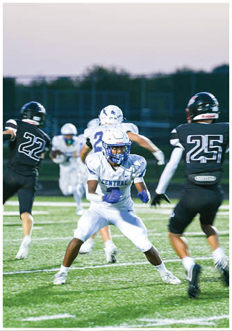 A group of people in football uniforms are actively playing on a field with one person in a black uniform jumping and another in a white uniform preparing to move. Description generated by AI