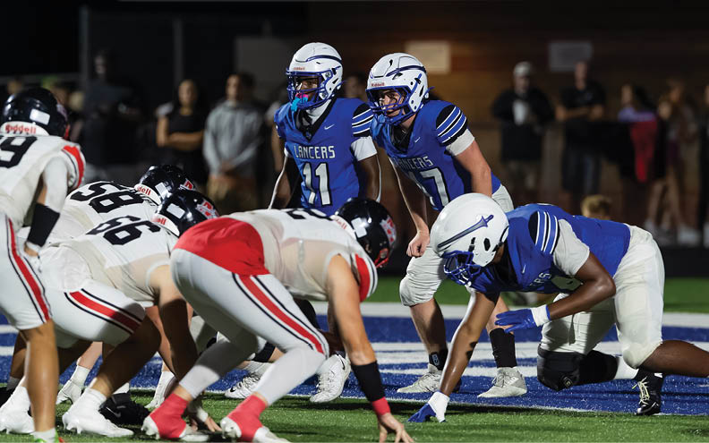 People in football uniforms are lined up on a field at night preparing for a play. Description generated by AI