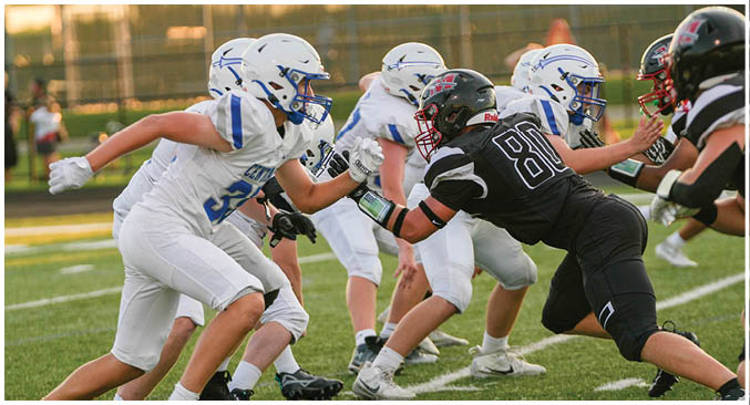 Several people in white and black football uniforms are engaged in a play on a green field with a football in mid-air. Description generated by AI