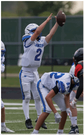 Three people in white and blue football uniforms are on a field with one person jumping and reaching to catch a football. Description generated by AI