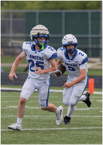 A person wearing a white and blue football helmet and uniform is looking to the side during a game or practice. Description generated by AI