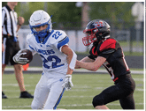 Two people in football uniforms are playing on a field with one person in white running while holding the ball and the other in black reaching to tackle. Description generated by AI