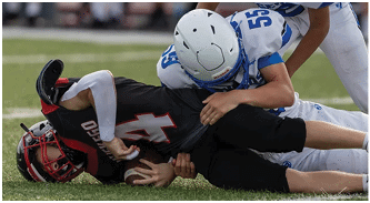 Two people in white and blue football uniforms and helmets are engaged in a play on a football field with blurred spectators in the background. Description generated by AI