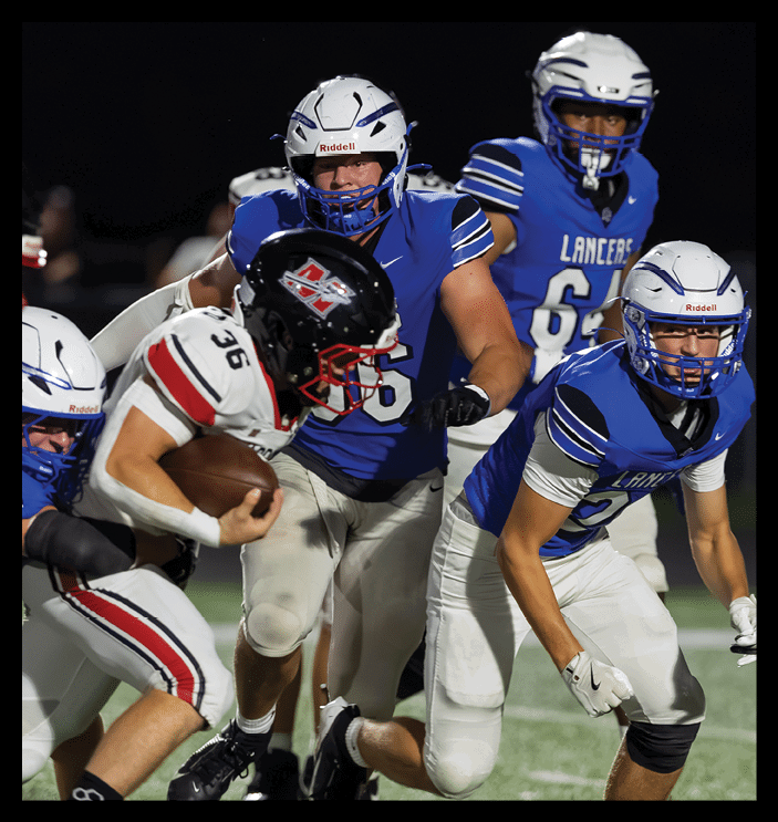 A person in a blue football uniform is attempting to tackle another person in a white football uniform who is holding a football during a nighttime game. Description generated by AI