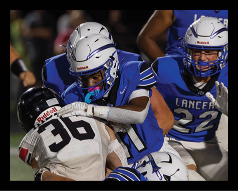 Two people in blue football uniforms tackle a person in a white football uniform during a game. Description generated by AI