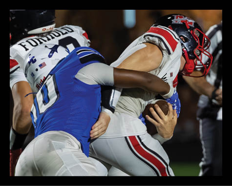 A person in a blue football uniform tackles a person in a white football uniform holding a football during a game. Description generated by AI