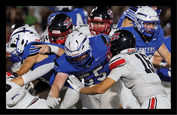 Several people in football uniforms are engaged in a close, intense play on the field during a game. Description generated by AI