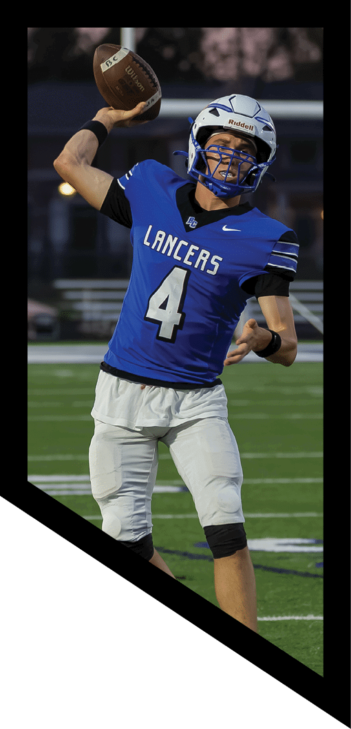 A person wearing a blue football jersey with the number 4 and a helmet is preparing to throw a football on a field with a scoreboard in the background. Description generated by AI