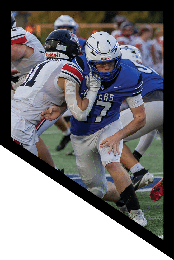 A person in a blue football uniform is running with the ball while being pursued by several people in white and black football uniforms on a grassy field. Description generated by AI