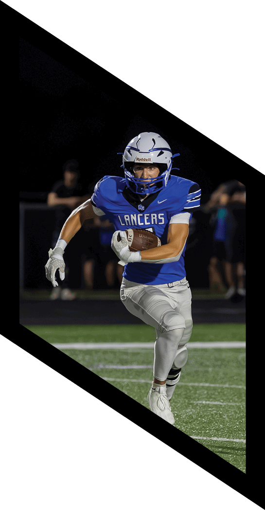 A person wearing a blue Lancers football jersey and white helmet is running on a field while holding a football. Description generated by AI