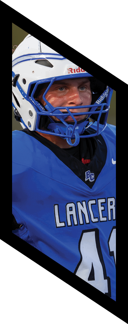 A person wearing a white and blue sports helmet and a blue jersey is shown against a blurred outdoor background. Description generated by AI