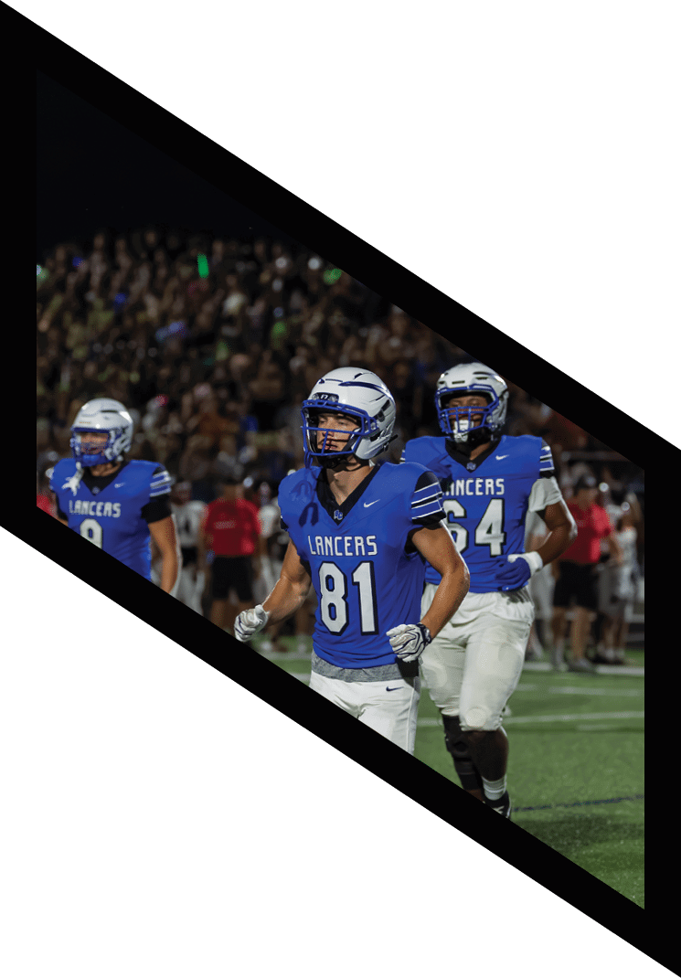 People in blue football uniforms are running on a field during a night game with a crowd in the background. Description generated by AI
