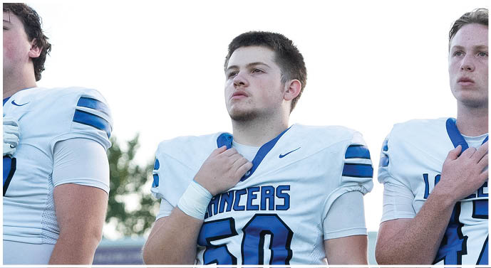 Three people wearing white football uniforms with blue accents stand side by side, each holding their right hand over their chest. Description generated by AI