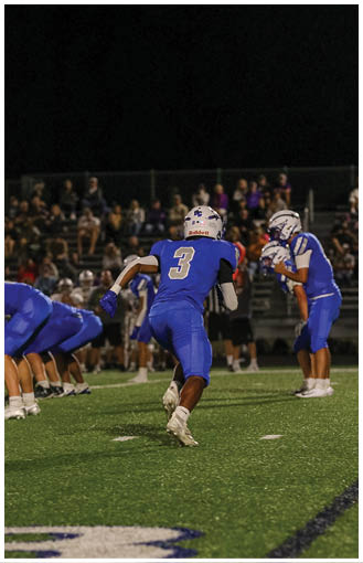 People in blue football uniforms are on a field at night with one person preparing to throw a ball and others in a ready stance. Description generated by AI