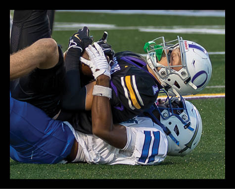 A group of people in black sports uniforms stand on a field with one person lying on the ground in front of them during a game. Description generated by AI