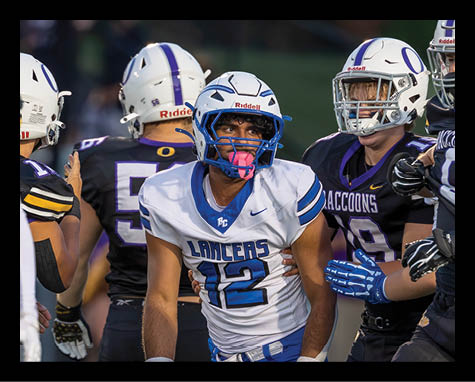 A person wearing a white football uniform with the number 12 and a blue helmet is being held by two people in black football uniforms during a game. Description generated by AI