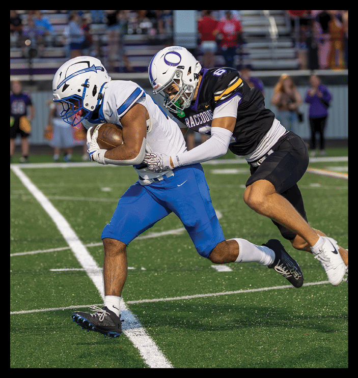 Two people in athletic clothing are playing football on a field, with one person running while holding the ball and the other attempting to tackle. Description generated by AI