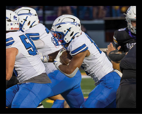 A group of people wearing blue and white football uniforms are actively engaged in a play on a football field with spectators in the background. Description generated by AI