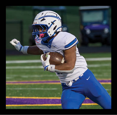 A person wearing a white football helmet and uniform is running on a field while holding a football tightly. Description generated by AI