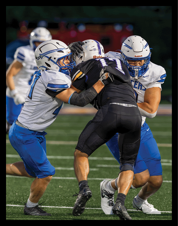 Two people in football uniforms are engaged in a tackle during a game on a grassy field. Description generated by AI