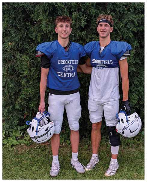 Two people wearing blue football jerseys with “Brookfield Central" printed on them stand side by side smiling in front of green foliage. Description generated by AI